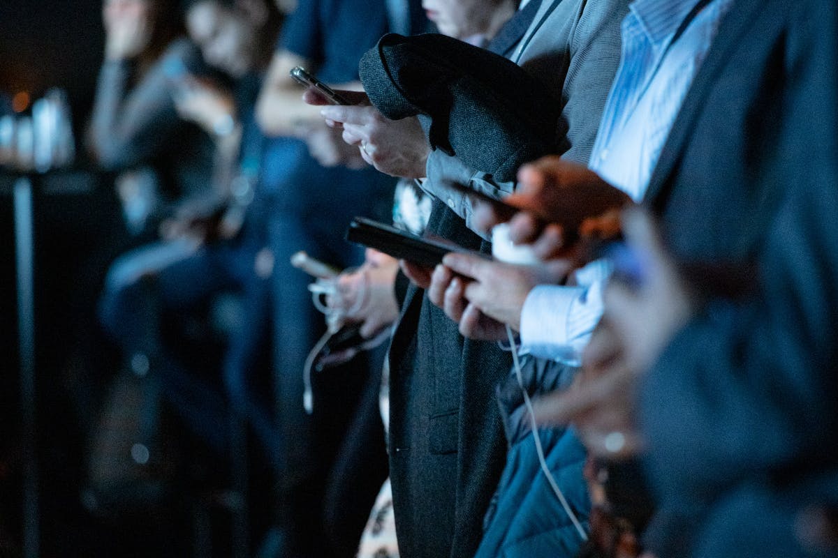 a line of people, showing mostly hands, all using their smartphones.