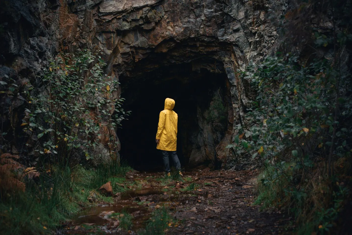 A person in a yellow rain slicker standing at the mouth of a dark cave