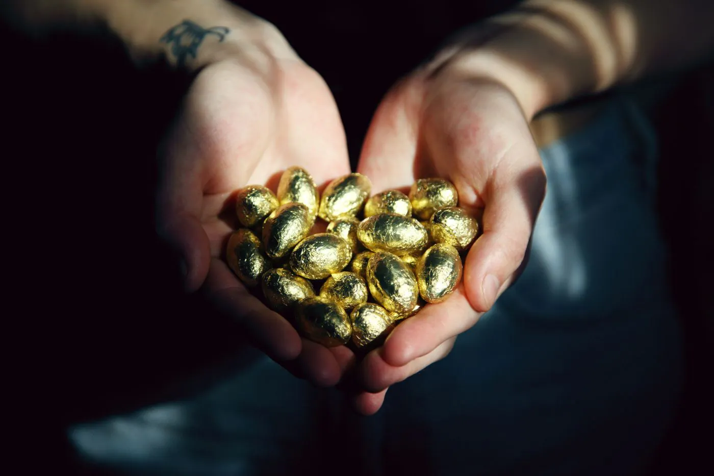 A person holding handfuls of small gold wrapped candy eggs