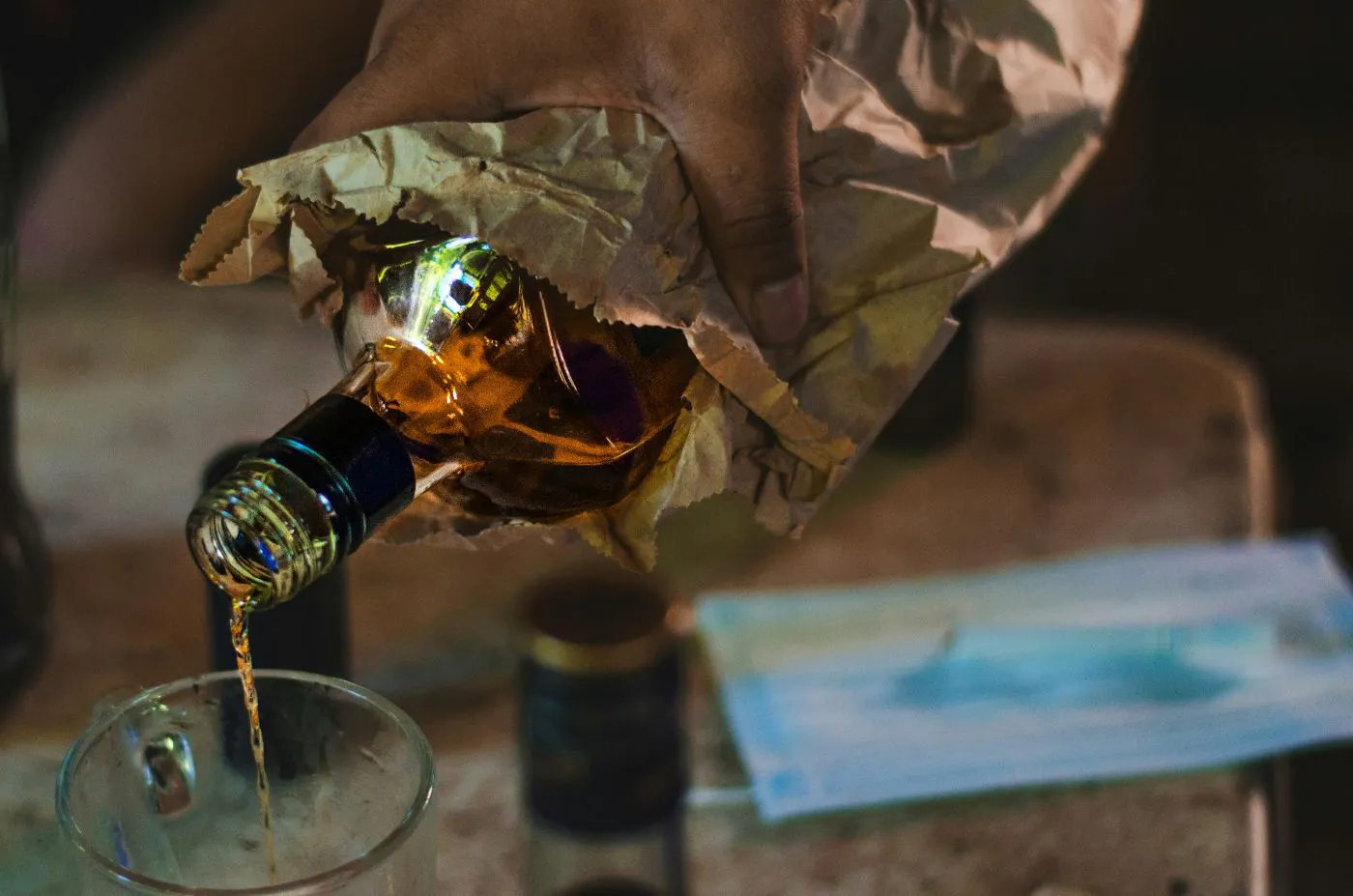 Whiskey being poured into a glass from a bottle wrapped in a paper bag