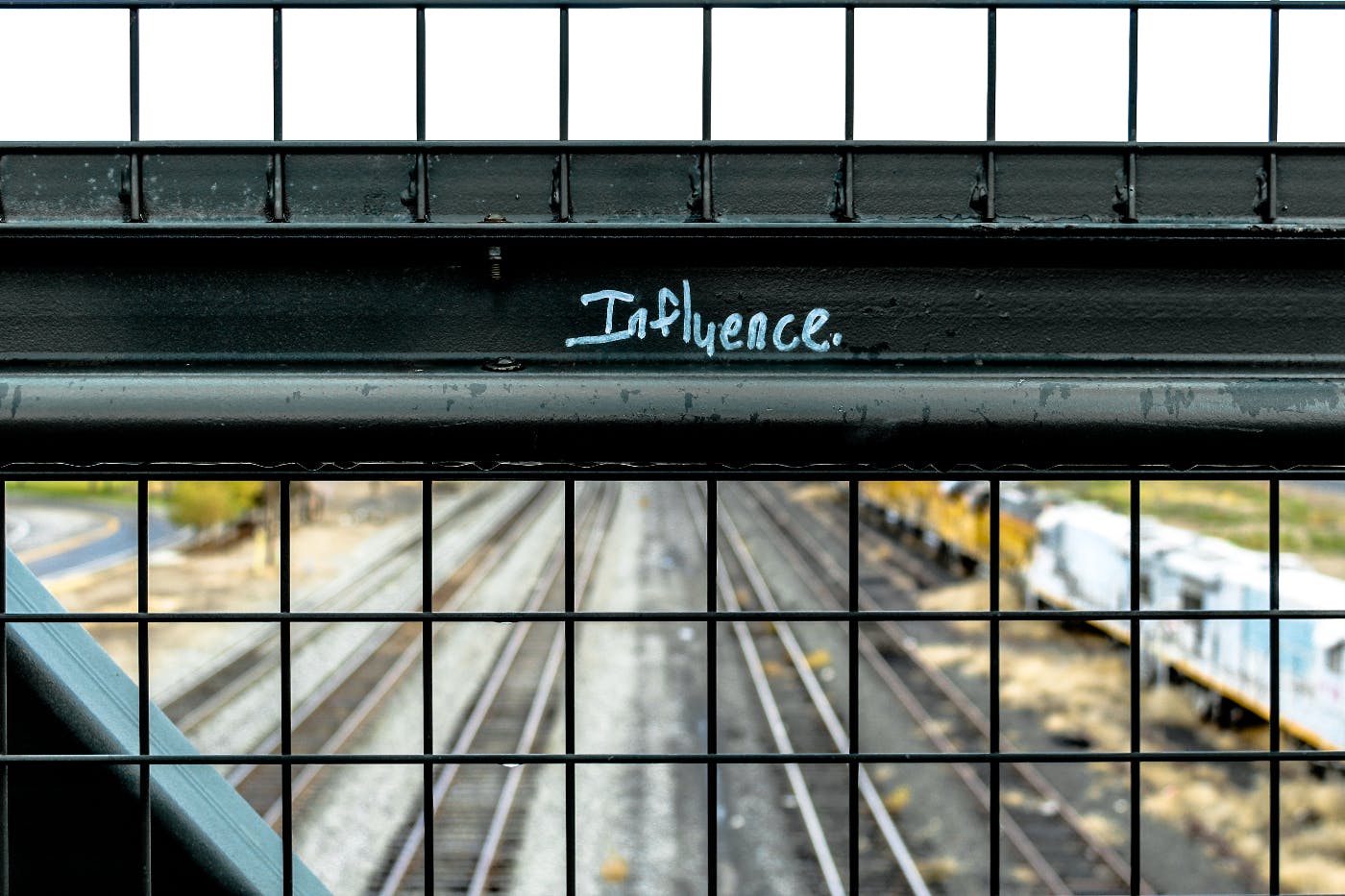 A train bridge with the word Influence in white on a railing