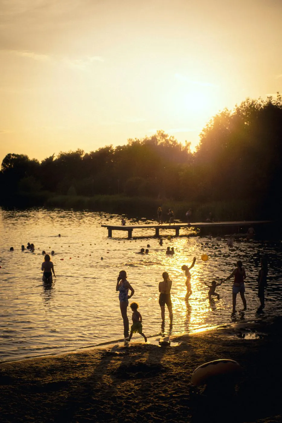 People playing on a beach near a lake at sunset