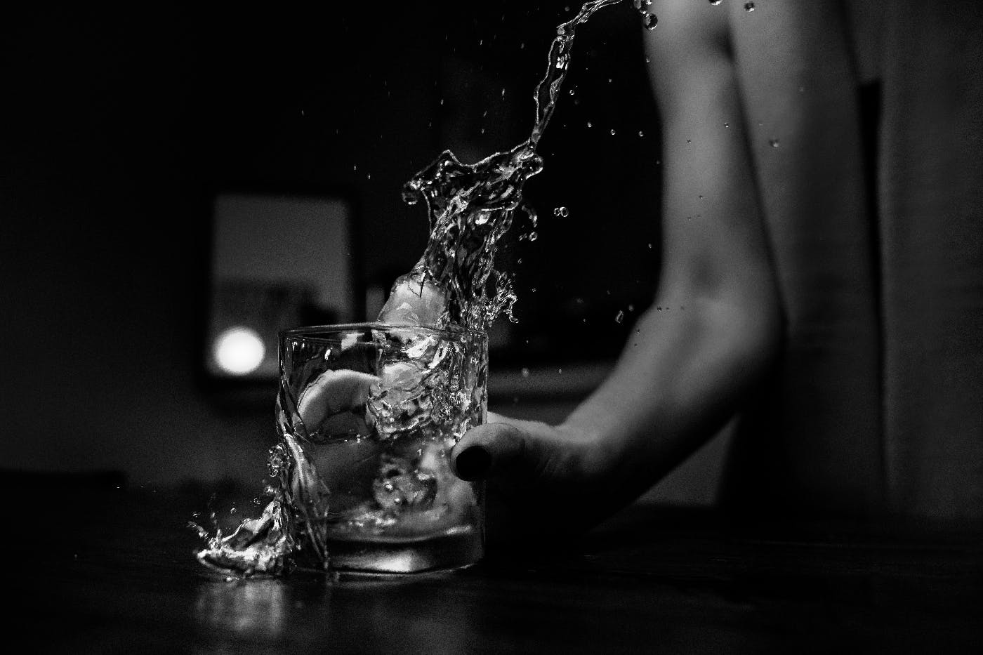 A woman pouring a glass of whiskey and missing the glass