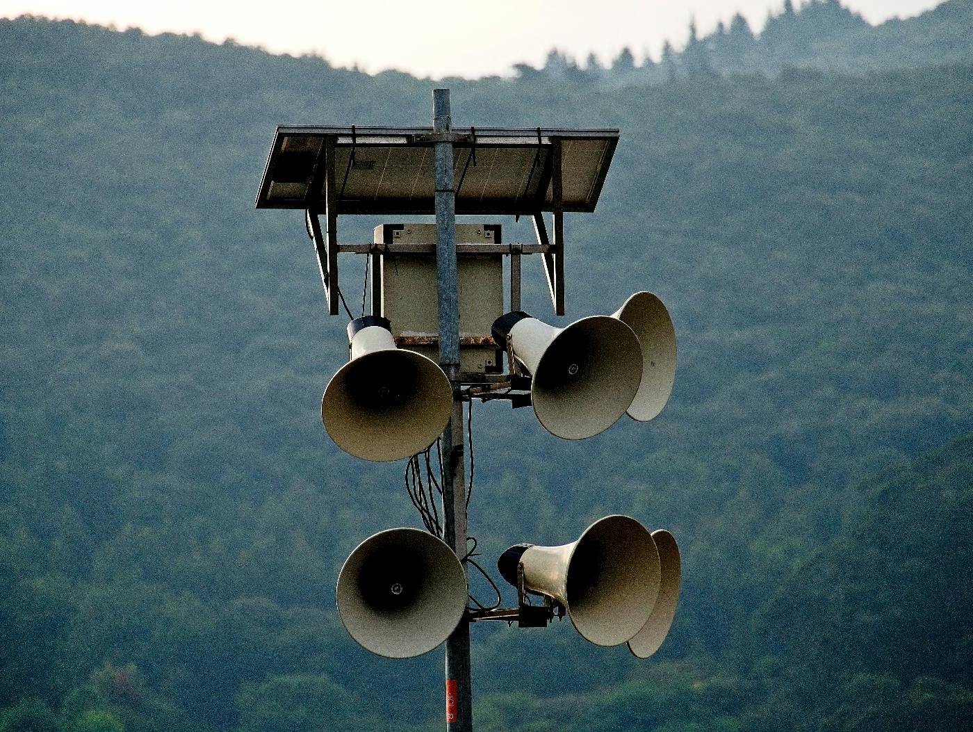 A pole with 6 megaphone speakers on it in front of a mountain