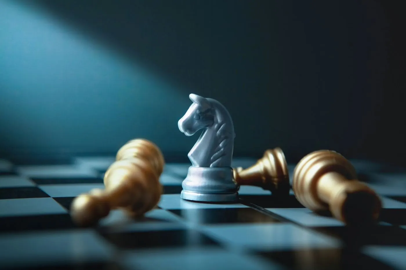 A white knight chess piece surrounded by three toppled pawns and one toppled Rook