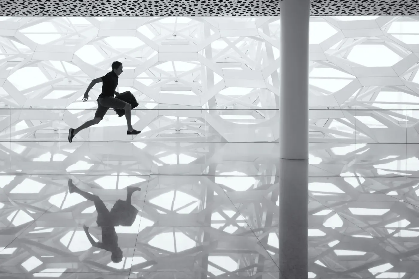 A man with a suittcase running across a reflective floor in an airport
