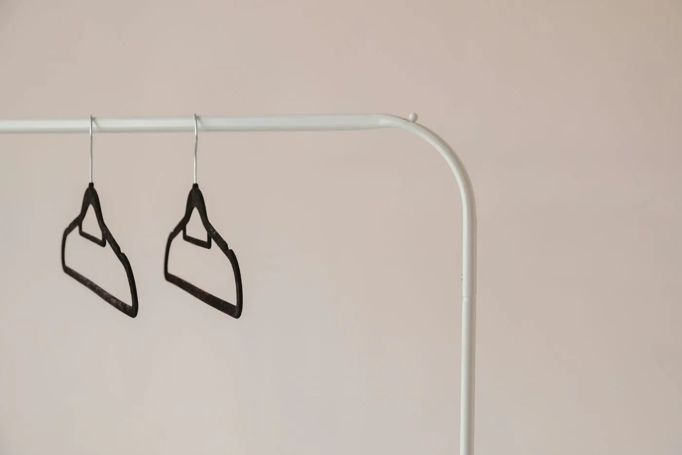 Two empty black hangers on a white rack