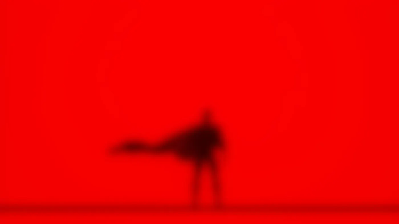 Silhouette of Superman, cape flowing against a red backdrop