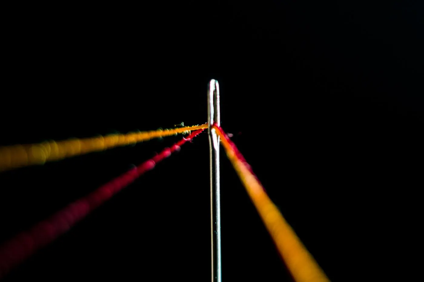 Yellow and red threads being pulled through the eye of a needle