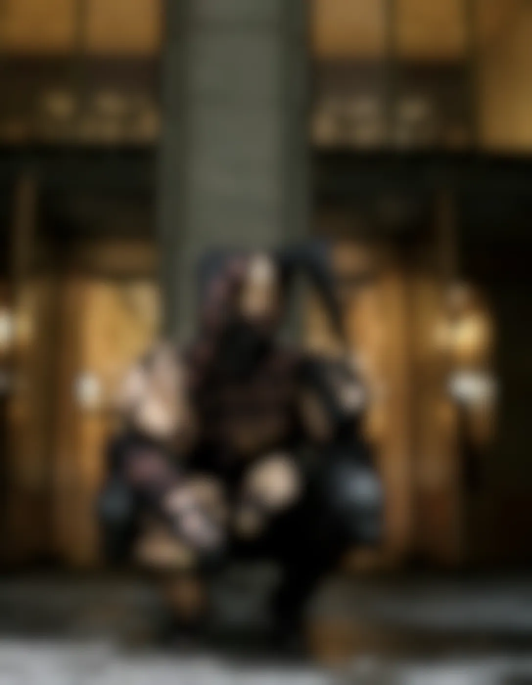 A person in black and gold motley crouching in front of a building
