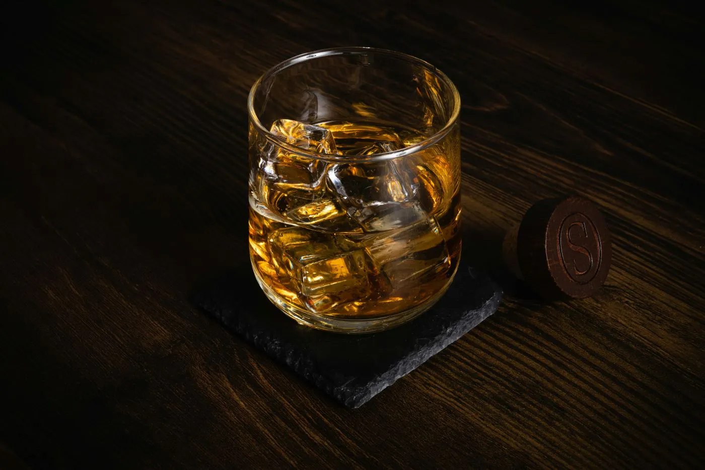 A glass of bourbon on a dark wood table