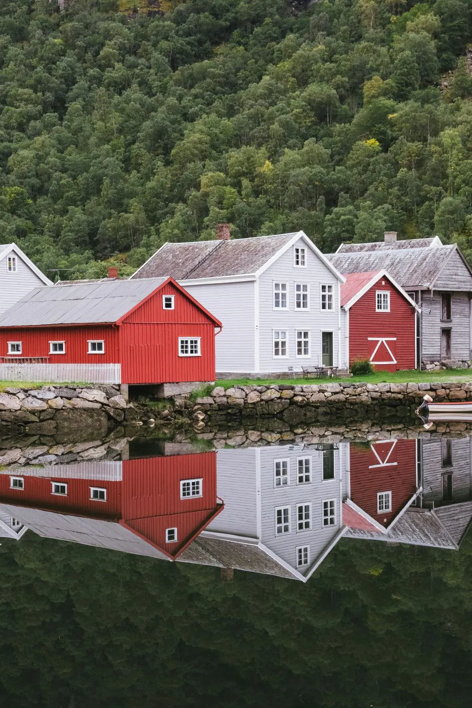 2 gray and 2 red structures along with a hill of trees mirrored in a body o fwater