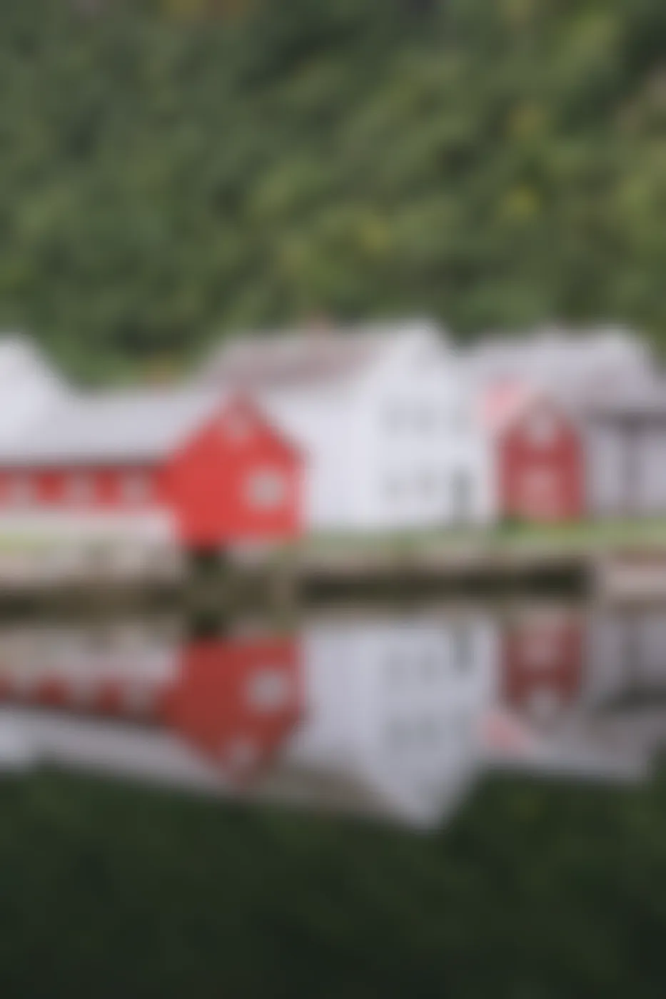 2 gray and 2 red structures along with a hill of trees mirrored in a body o fwater