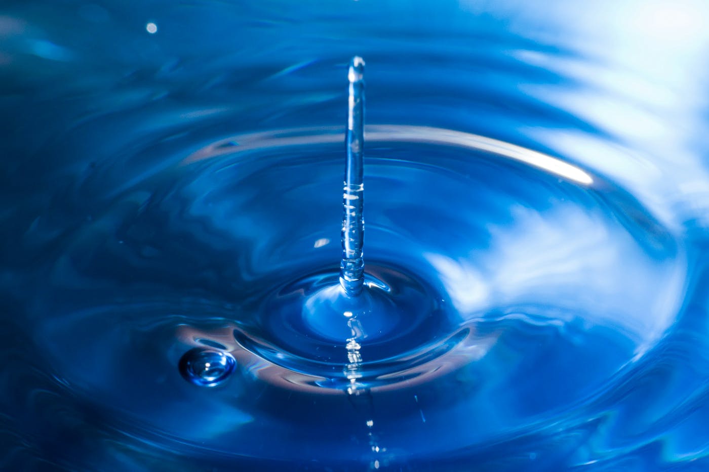 a water drop hitting and rebounding in a blue pool