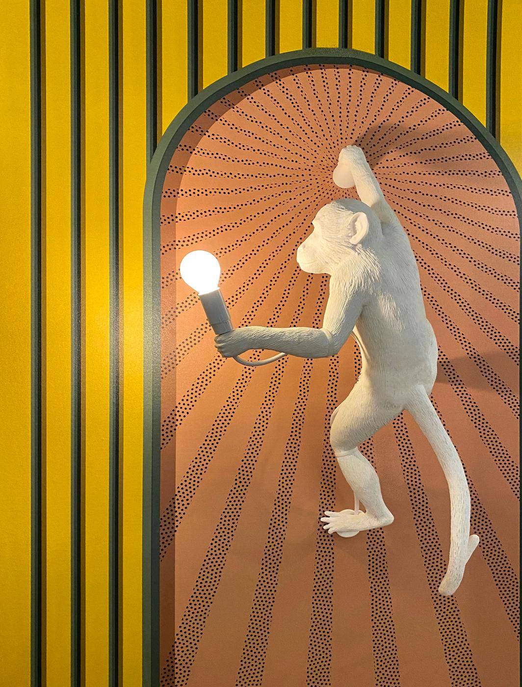A plaster monkey climbing a wall holding a light bulb