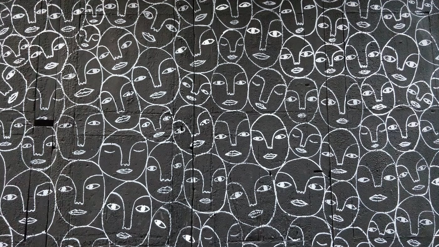 A black wall with chalk drawings of hundreds of very similar faces