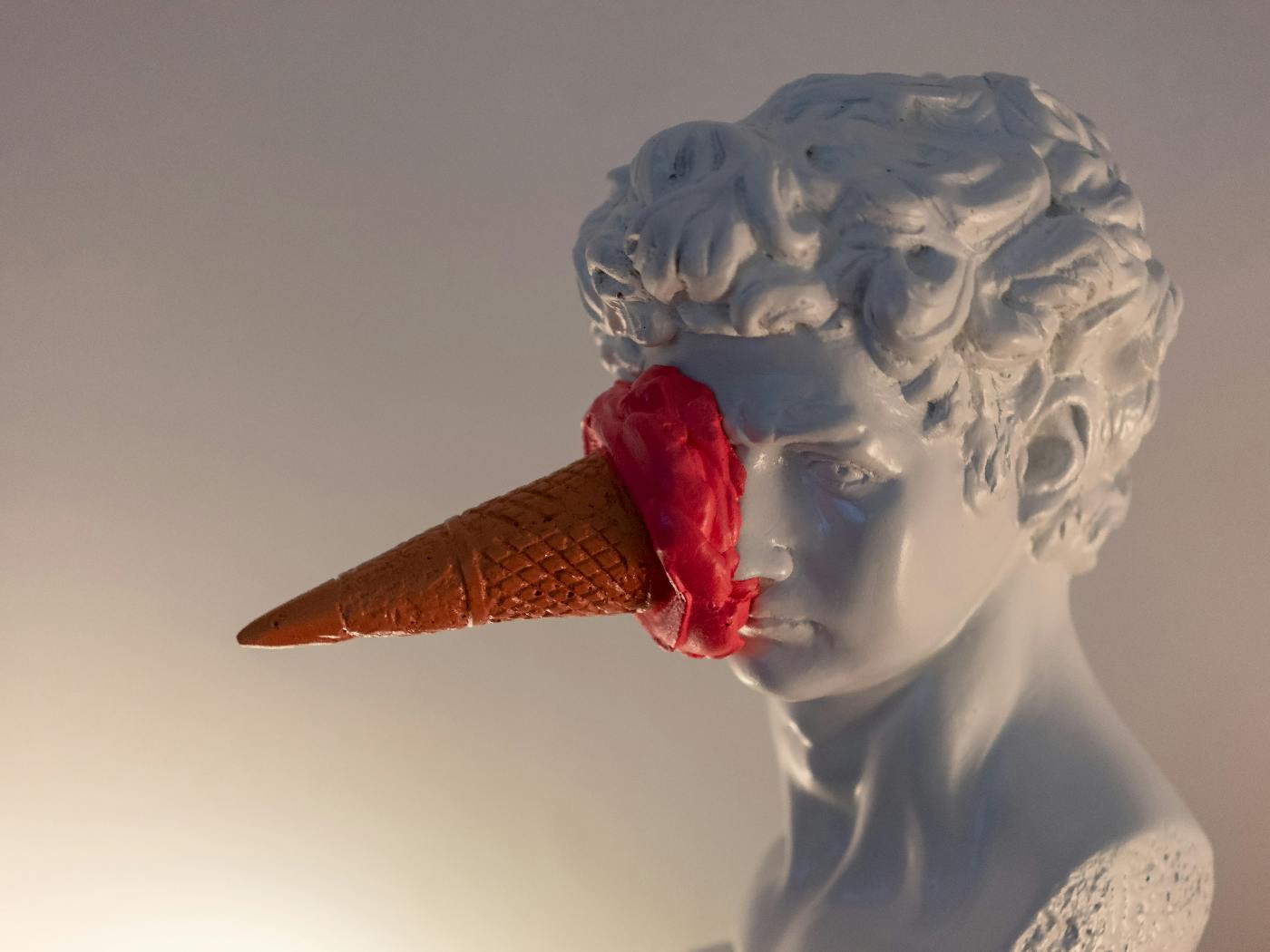 The marble bust of a man with a red ice cream cone stuck to his face