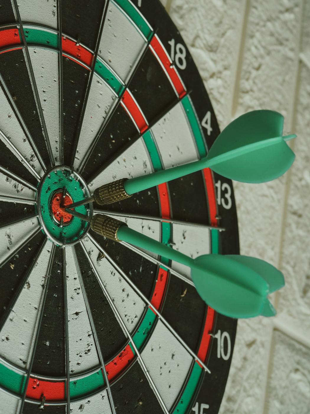 A dart board with two green darts in the bulls eye