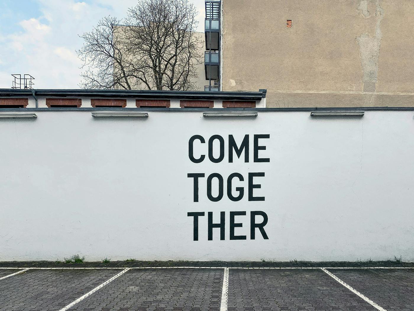 A white wall in a parking lot with Come Together painted on it