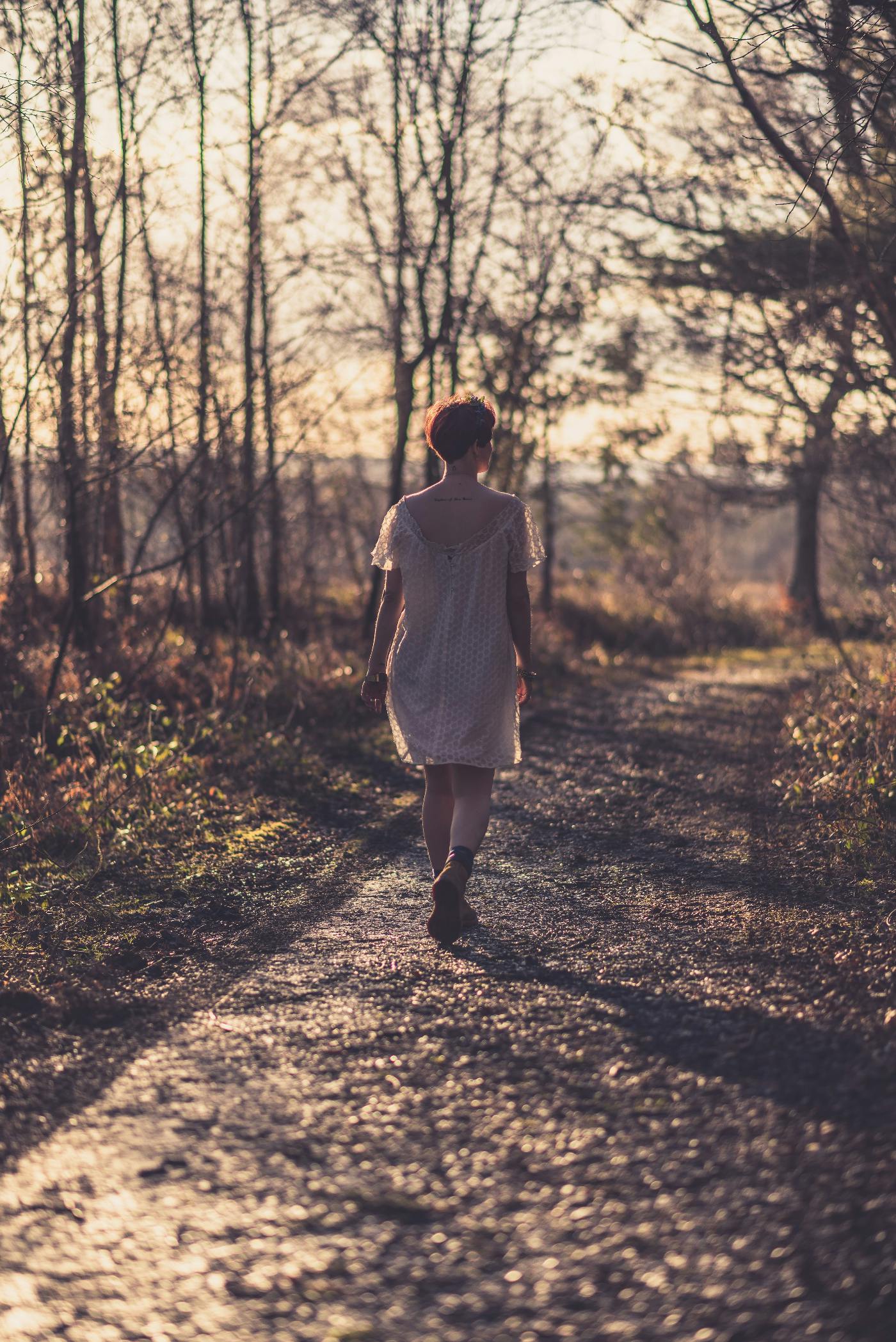 a woman in a white gauze dress walking a path in the woods.