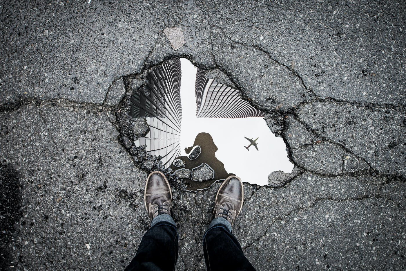 A pot hoel filled with water reflecting a person, buildings and a plane