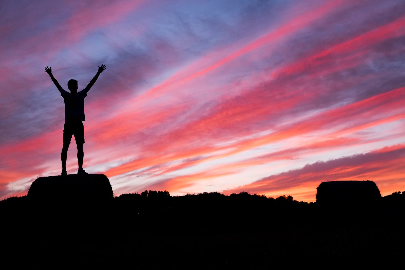A man, arms raised standing atop a rock in silhouette in the sunset
