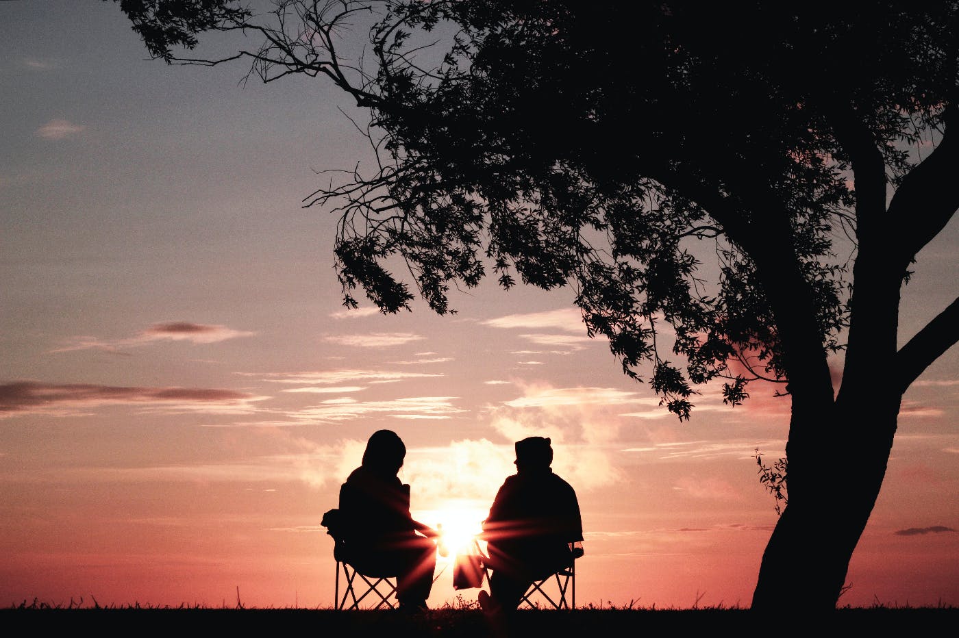 Two people in silhouette under a tree at sunset having a conversation.