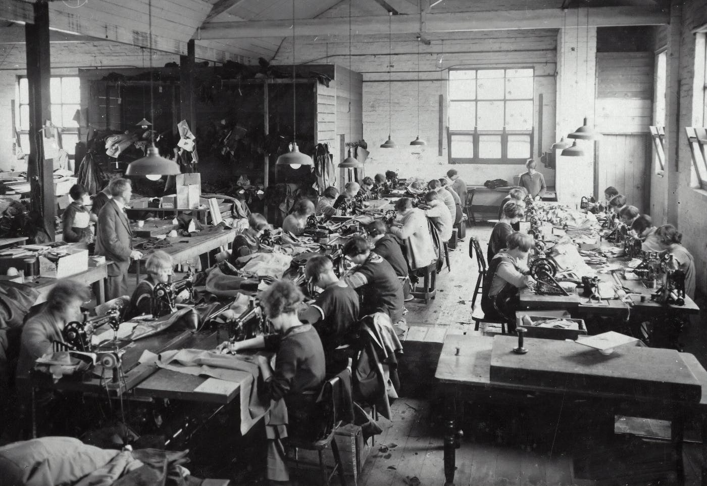 A Victoriam era sweat shop with women and kids at sewing machines.
