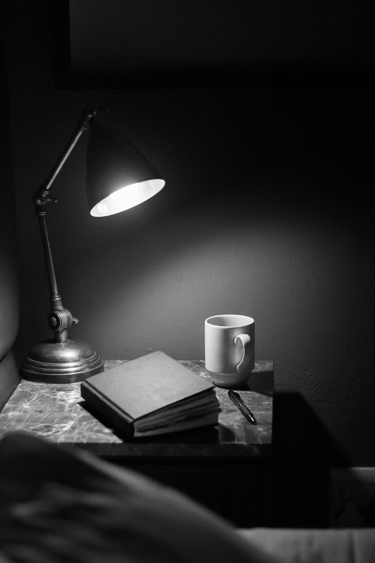 a bedside table with a lamp, a coffee cup and a journal in black and white