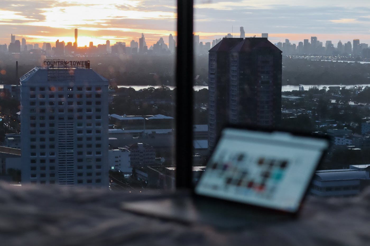 The view from a window of a city and a laptop in the forground.