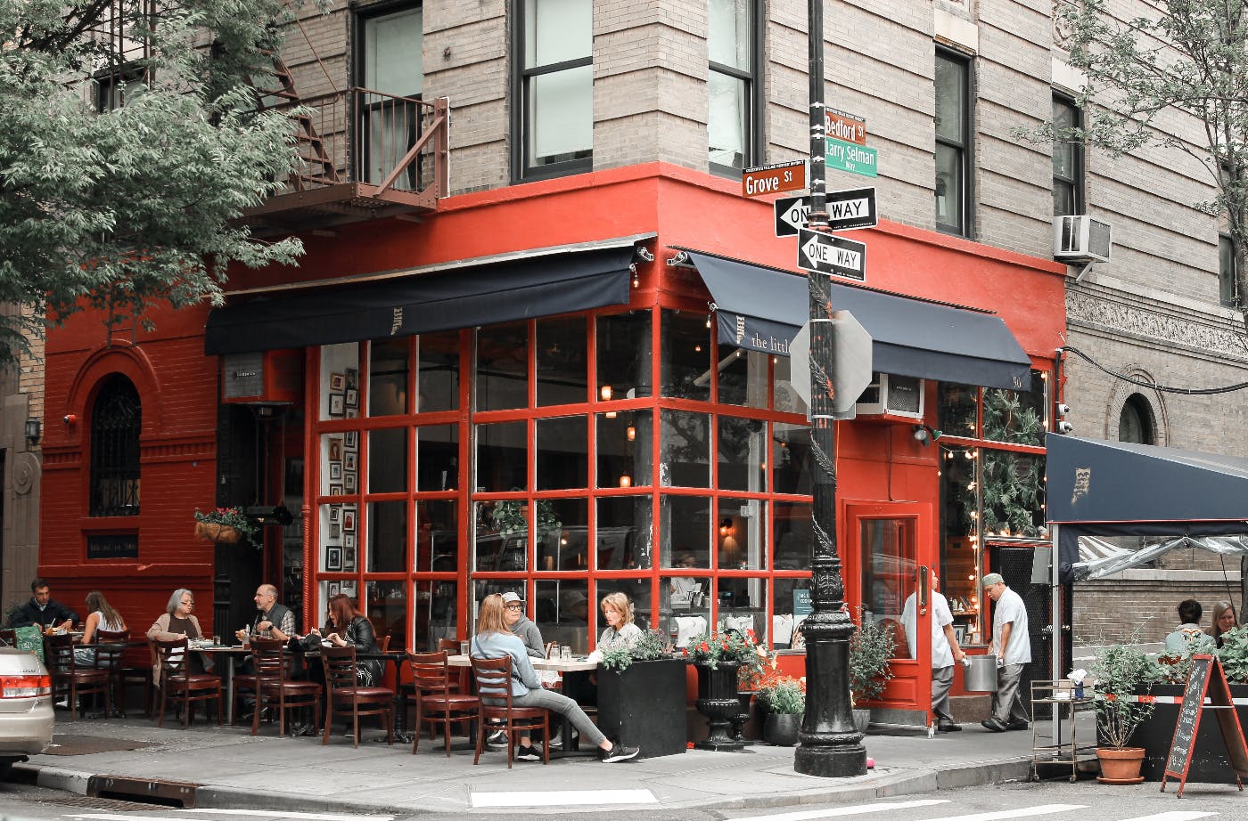 Outside of a corner coffee shop, with red walls and people at tables.