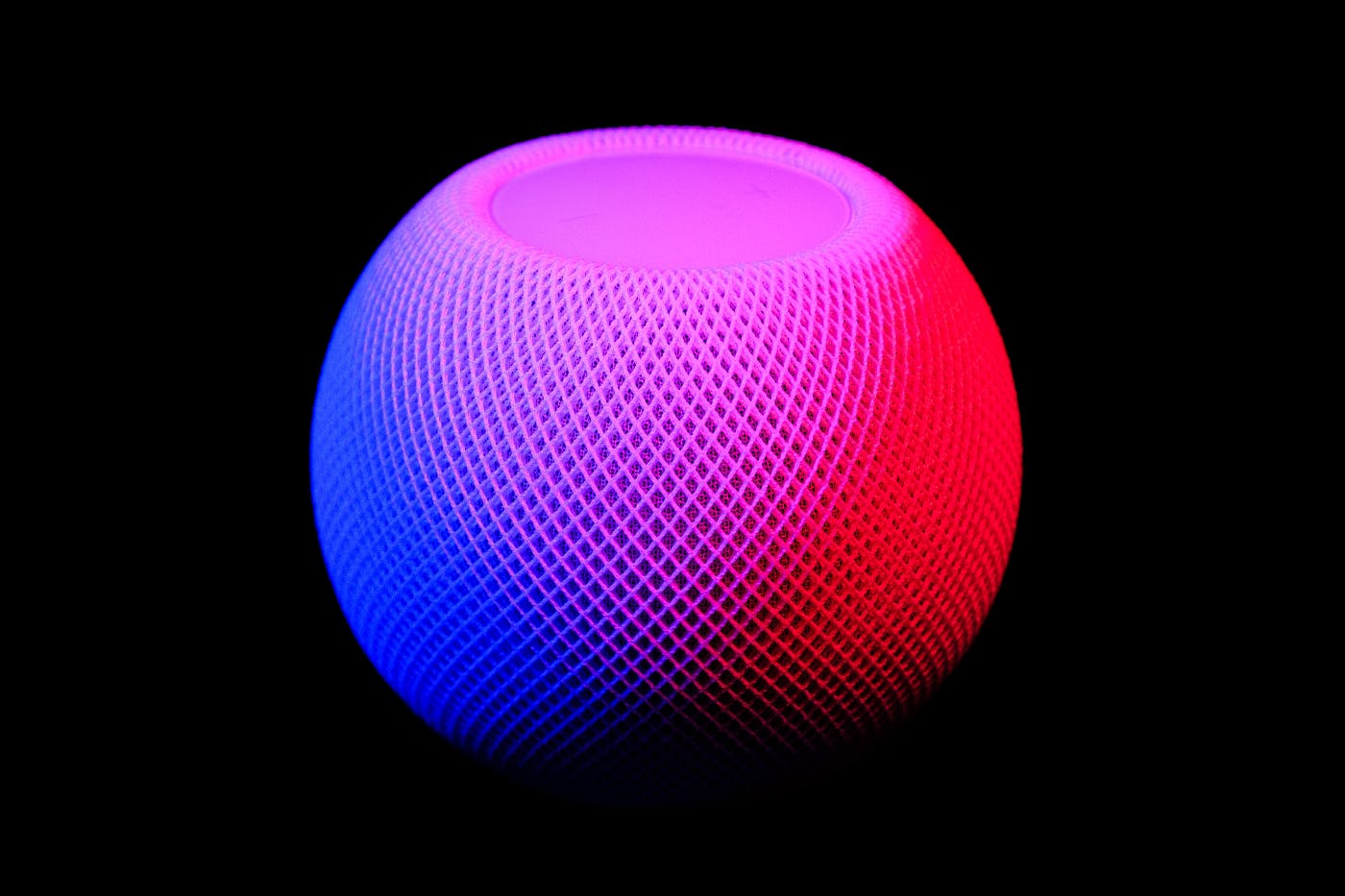 A blue, pink, and red Alexa speaker against a black background