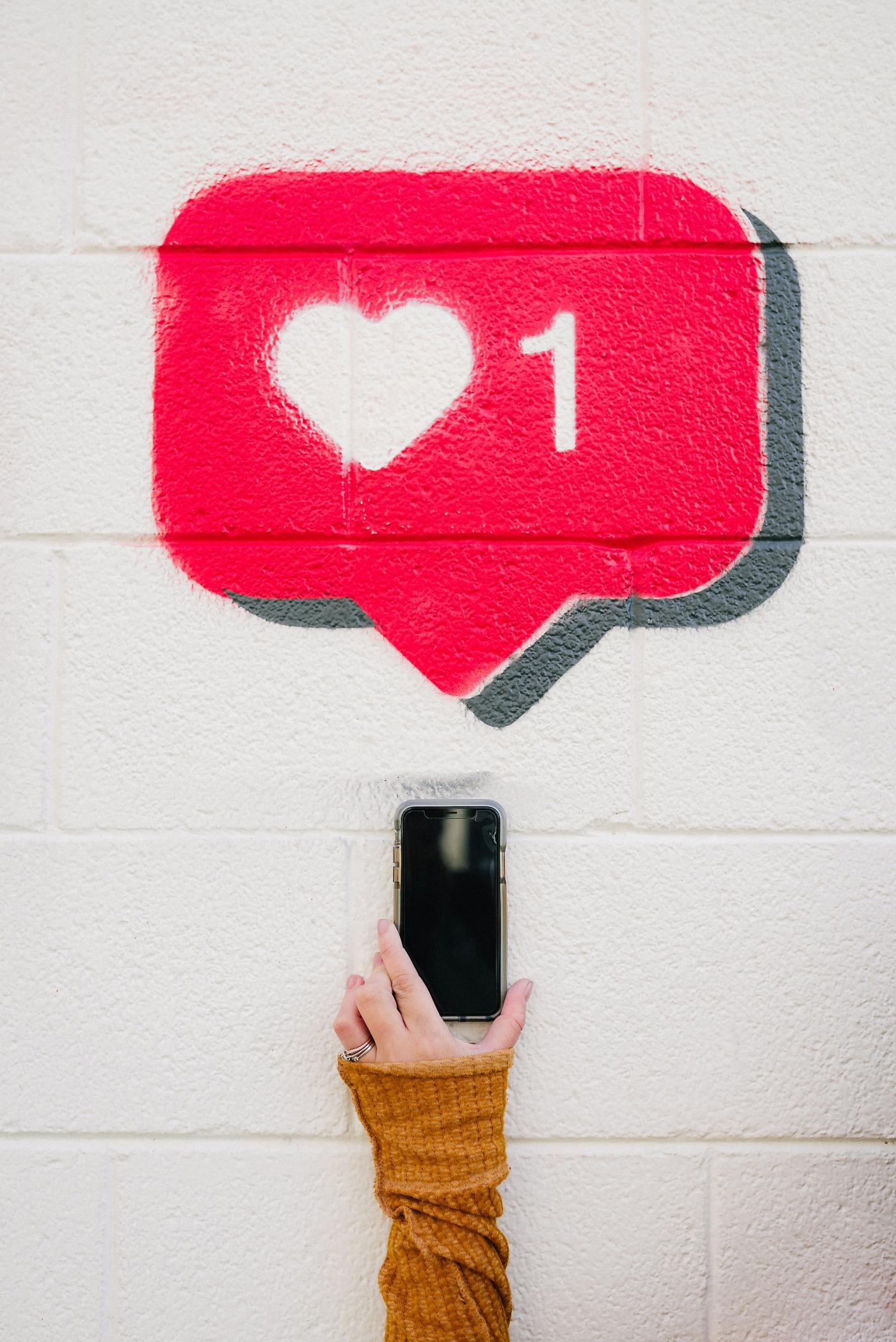 A wall with a heart and the number one painted on it, with a woman's hand holding a phone under it.