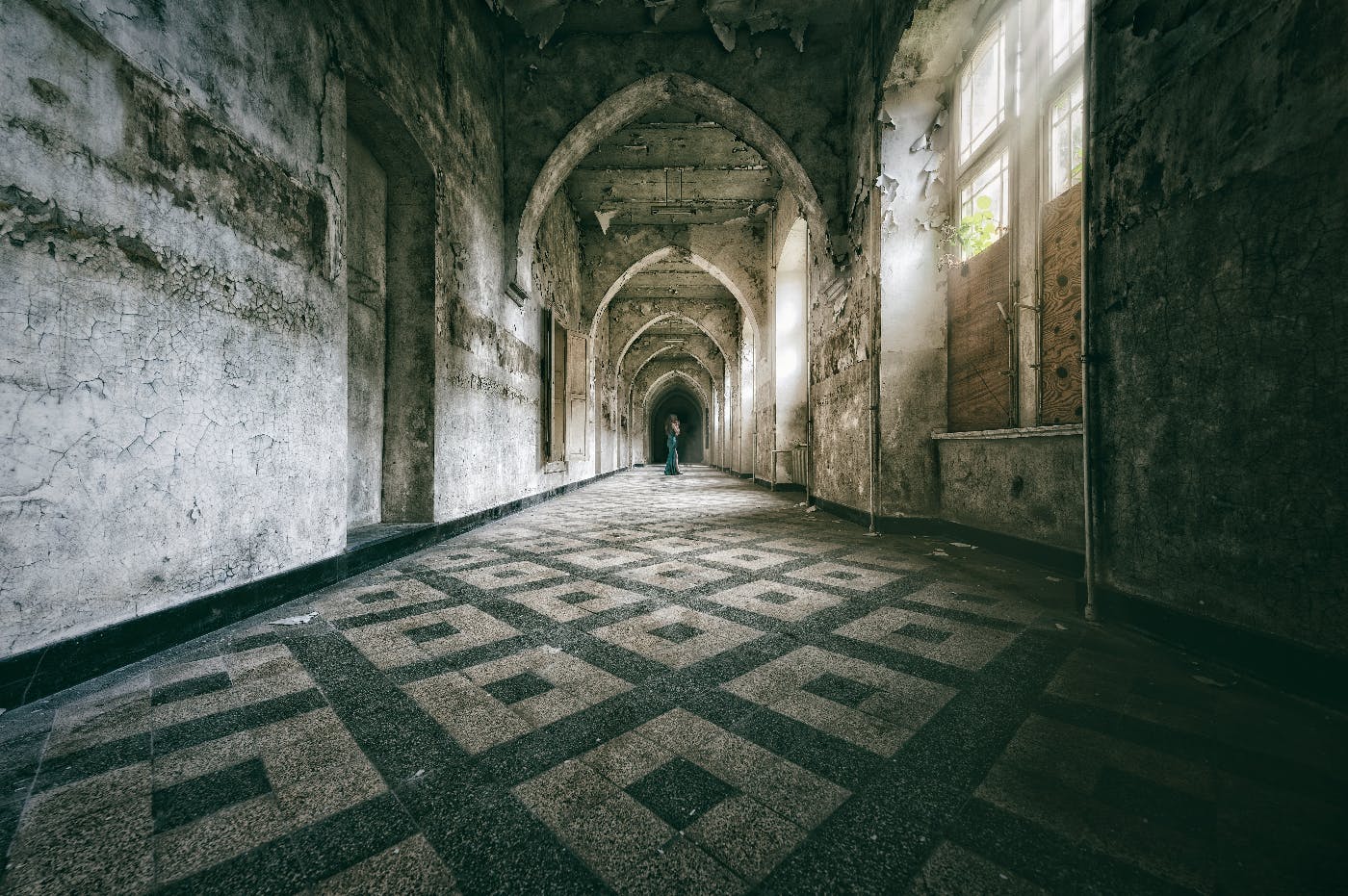 a woman in a green dress standing at the far end of an ancient hall