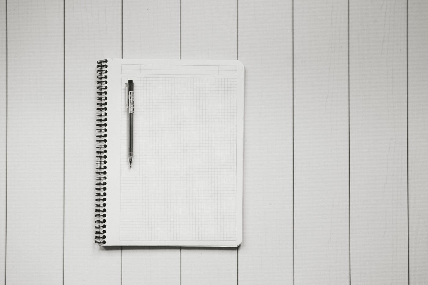 a blank notebook page with a black pen on a slat board table