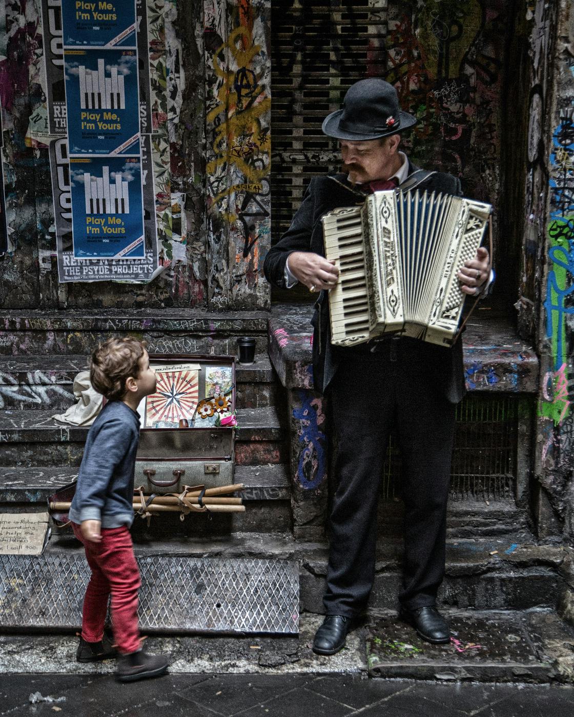 A busker playing accordian looking at a boy