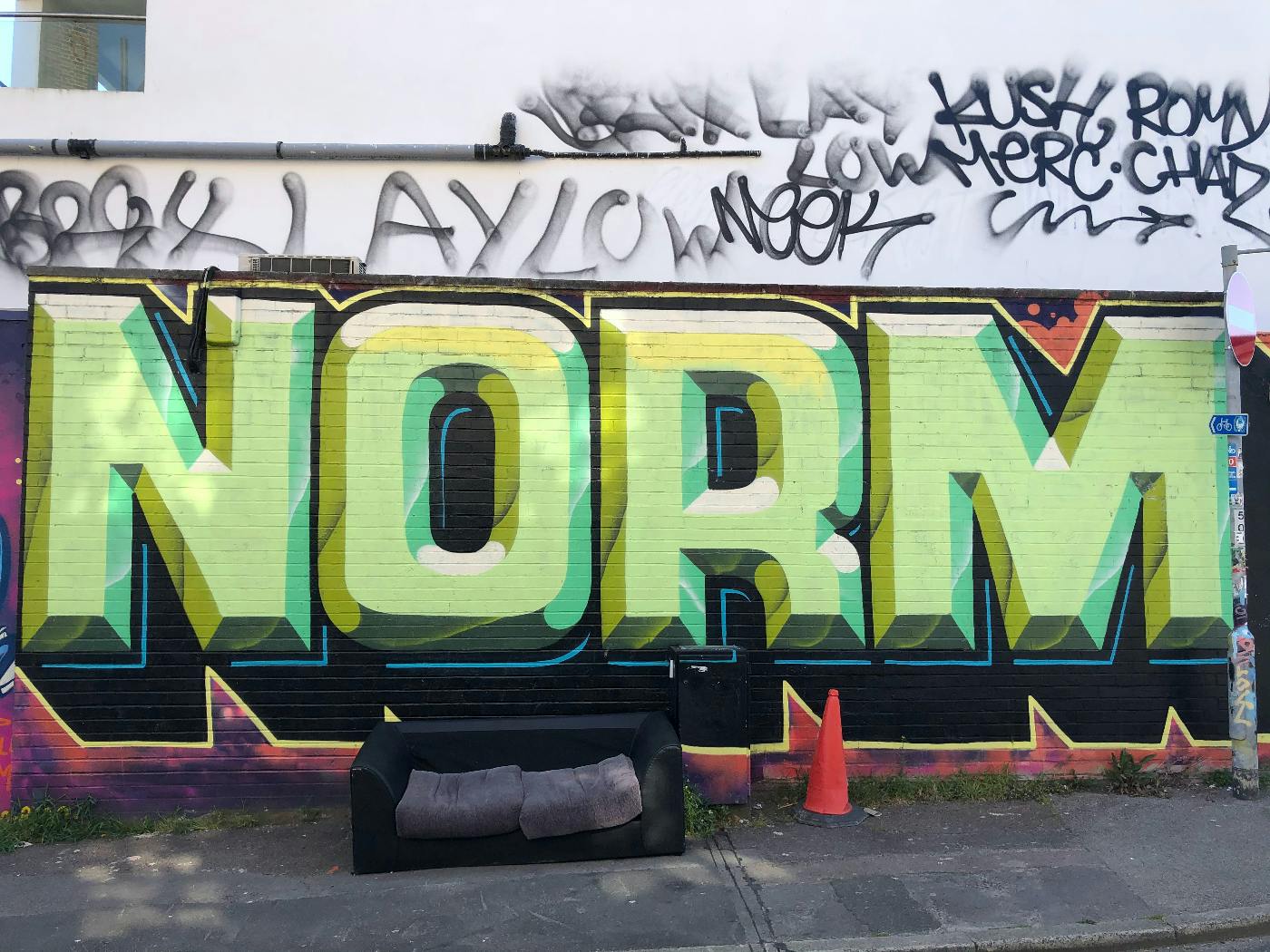 a sofe on a street in front of graffiti that says NORM