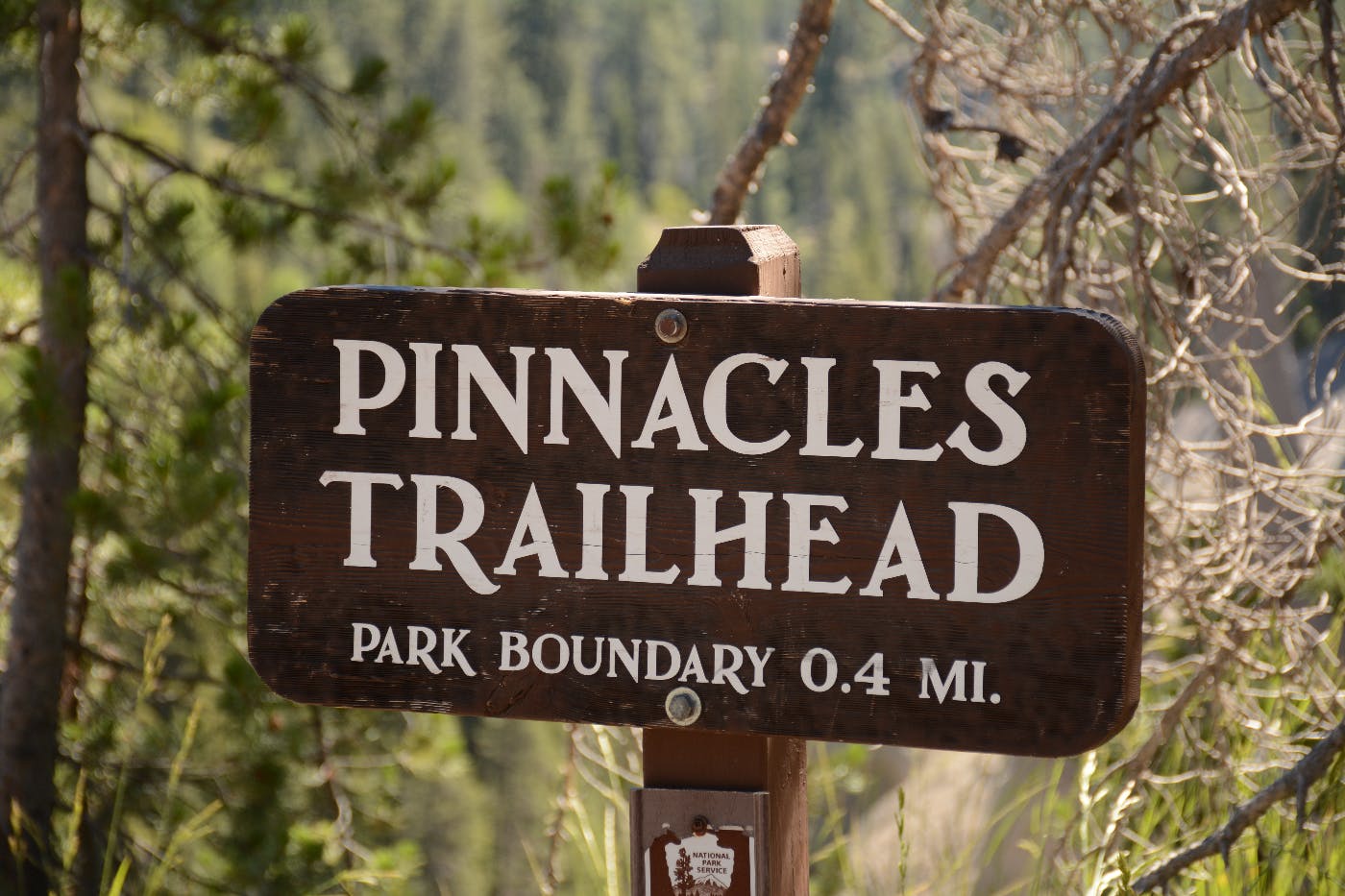 A brown wood sign with white letters reading: Pinnacles Trailhead Park Boundary 0.4 MI