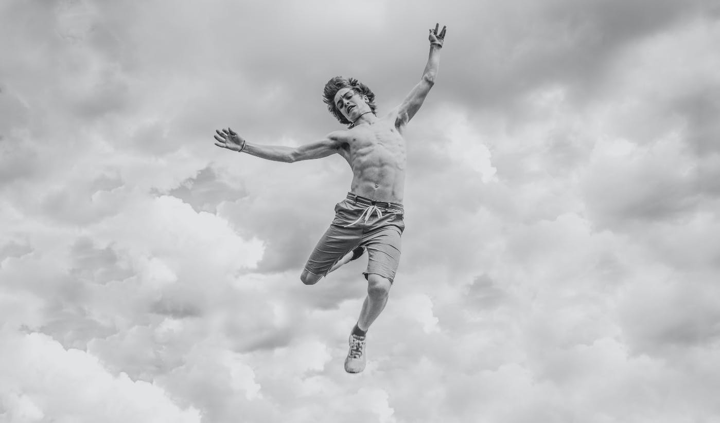 A young man, stripped to the waist, flying through the air against a cloudy background.