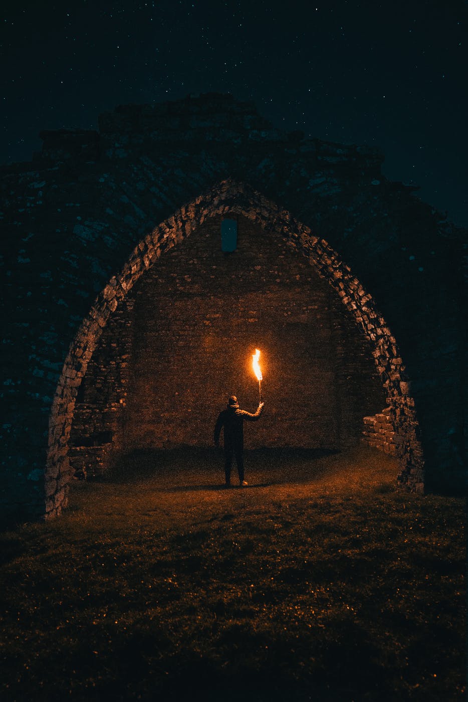A man with a torch standing beneath an underground stone arch