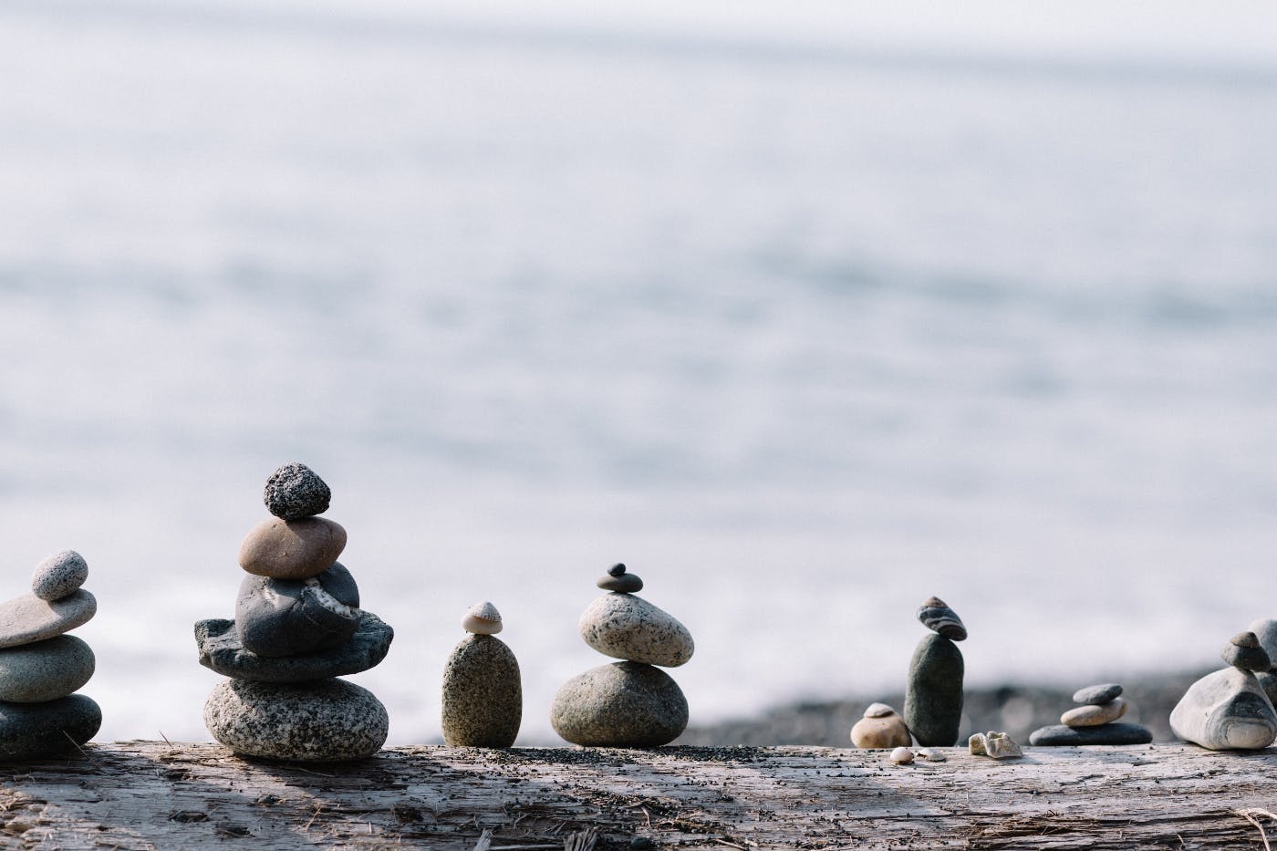 rows of stones balanced on top of each other on a log by the sea