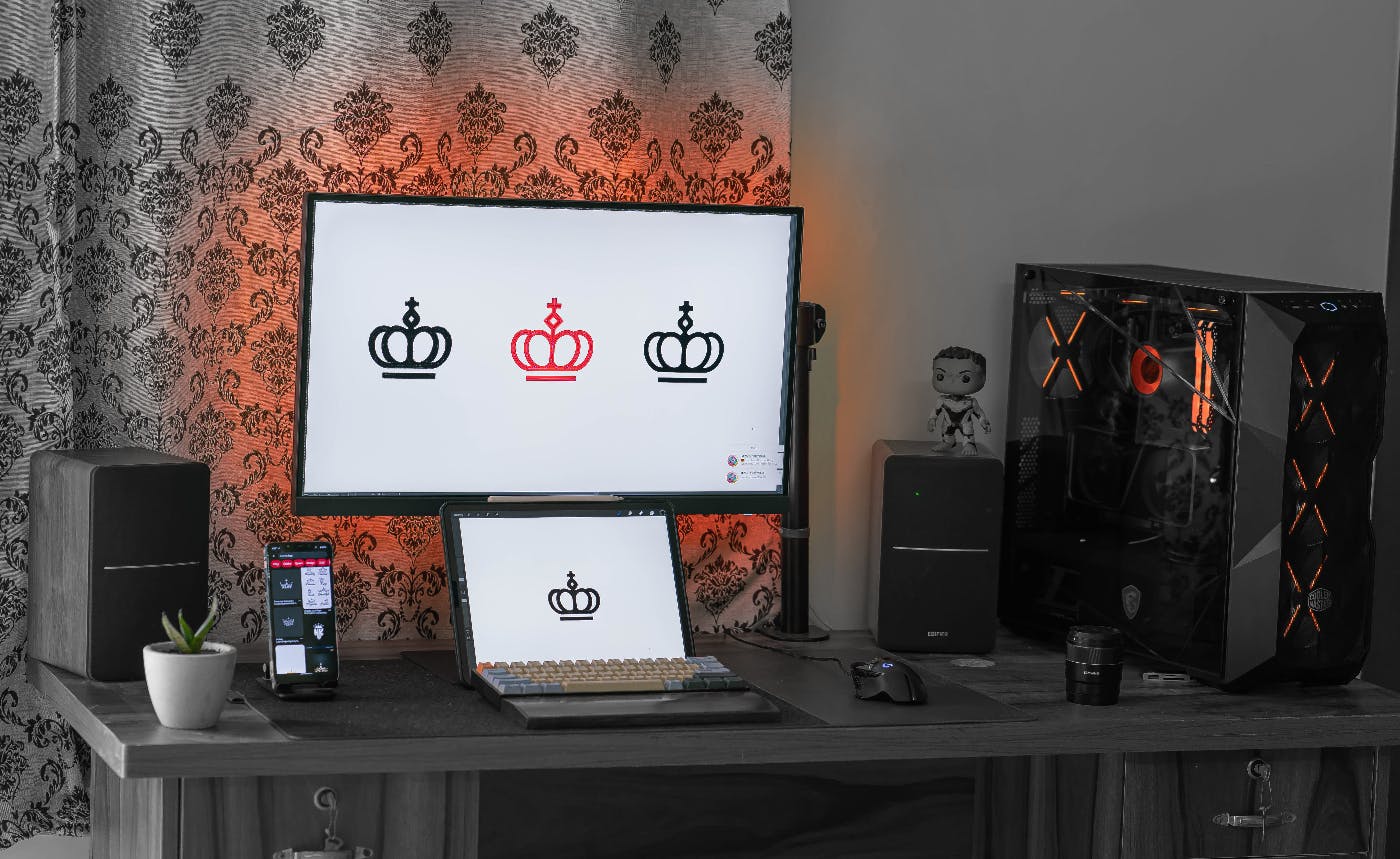 A laptop and a large monitor with designs for a crown type logo on them