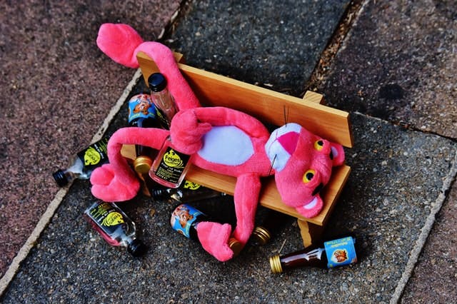 pink panther stuffed animal on bench surrounded by beer bottles