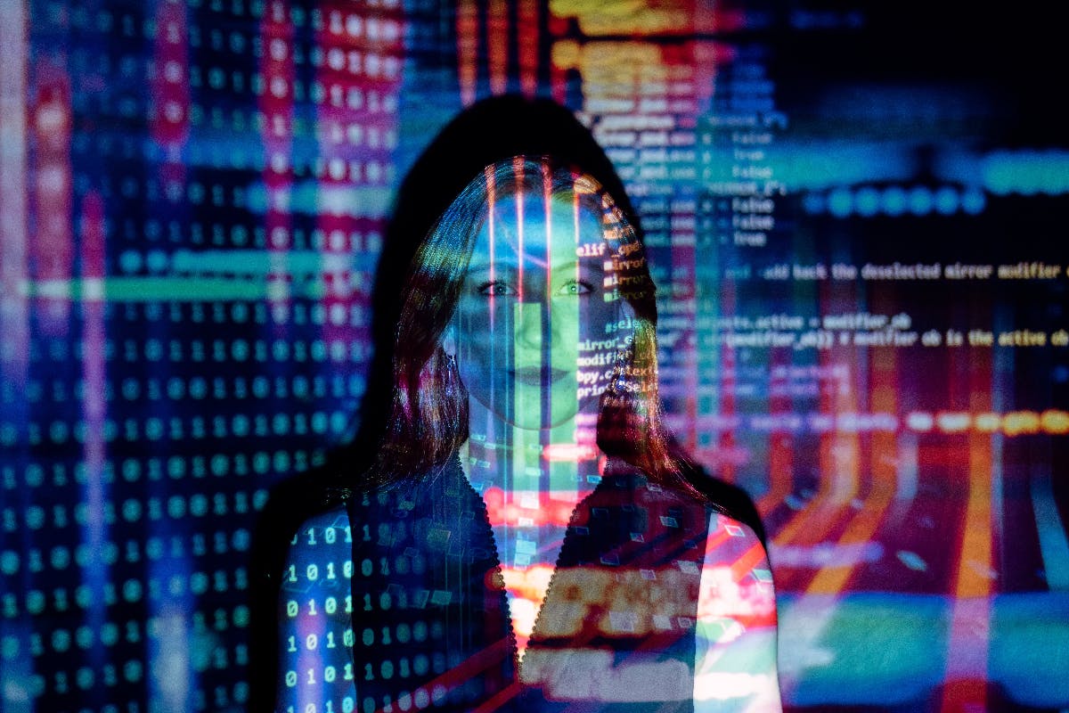 woman standing in the light of a computer  screen with data projected on her image.