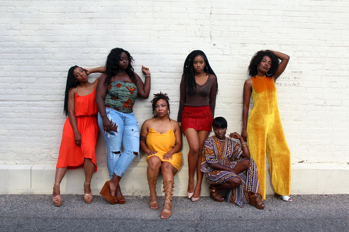 Six women leaning against a white wall