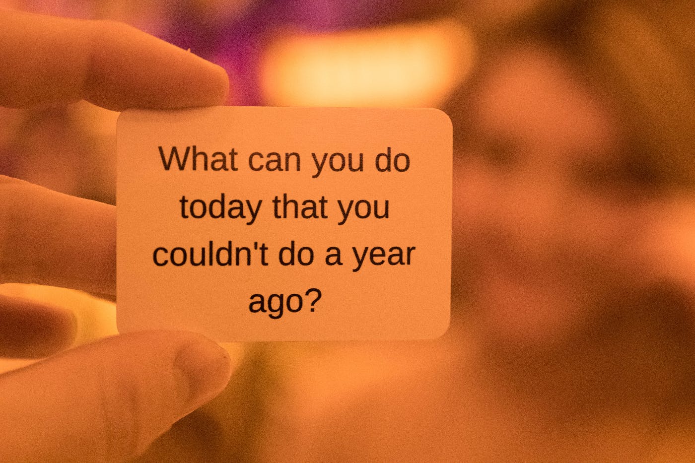 A hand holding a small card that reads What can you do today that you couldn't do a year ago?