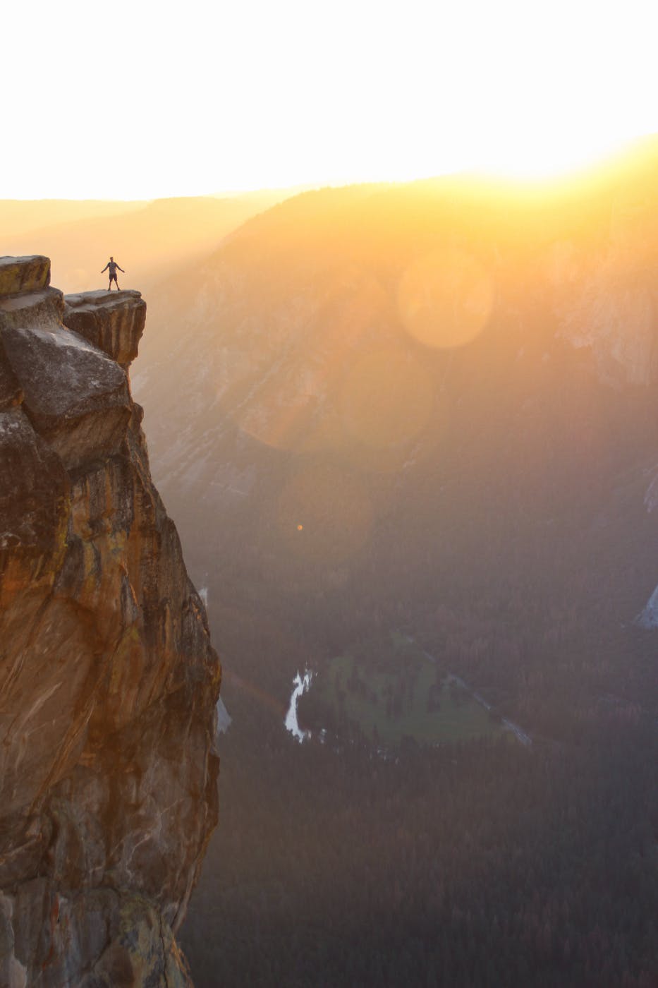 a man standing at the edge of a rock jutting out over a vast canoyon