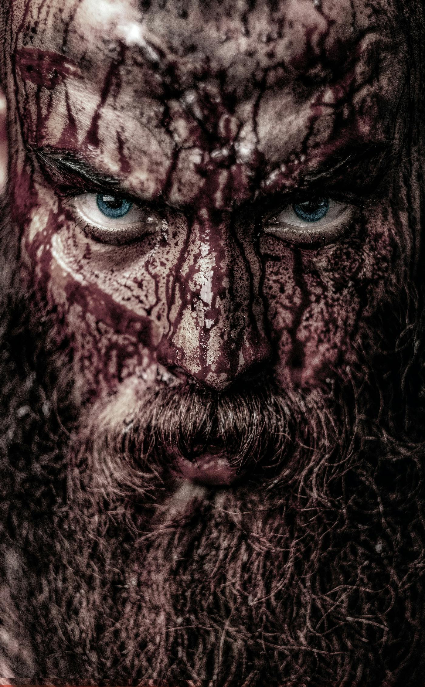 close up of a bearded man with blue eyes covered in blood