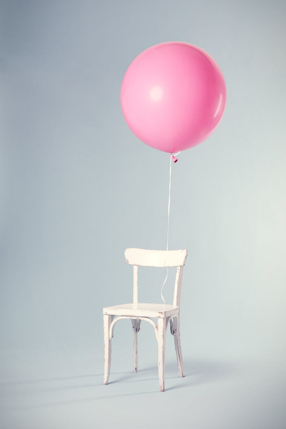 A white wood chair with a large pink balloon tied to it