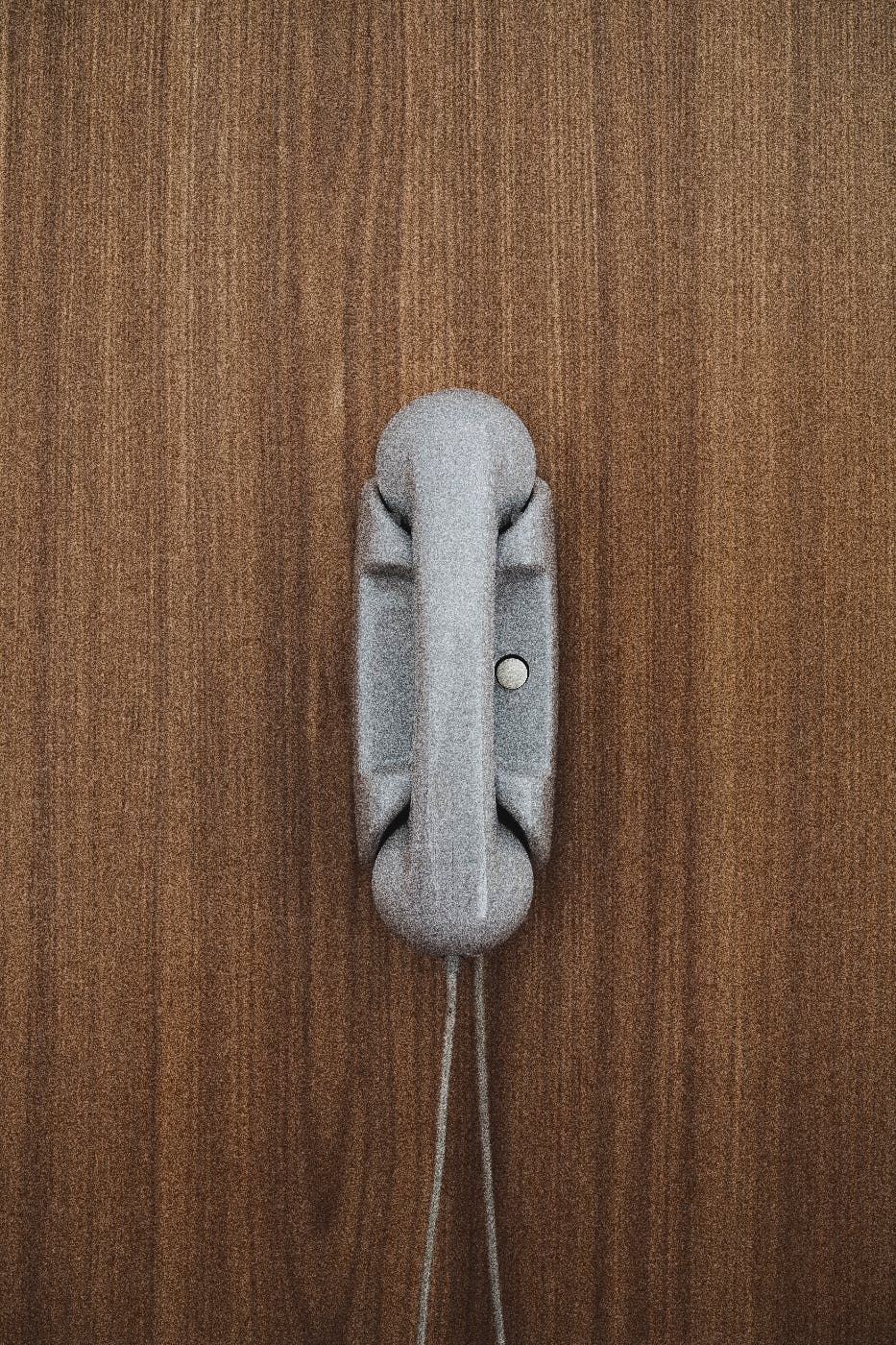 a gray phone with one button hanging on a wood panel wall